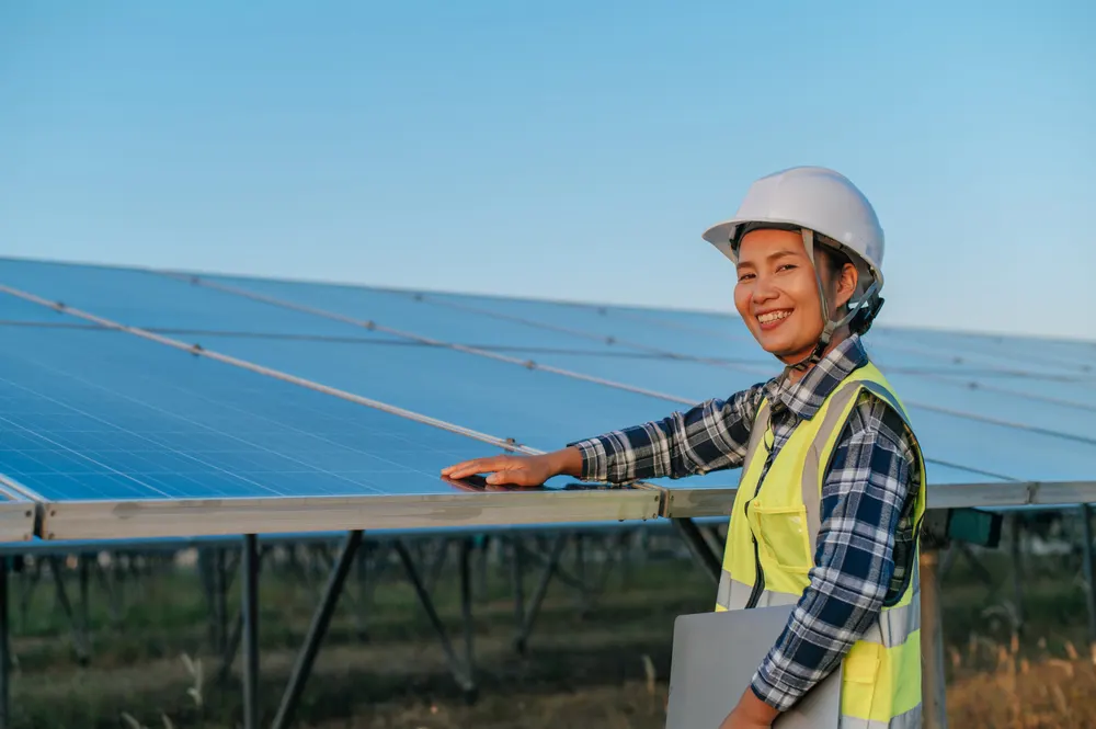 An engineer in a hard hat and hi-vis checking a row of solar panels